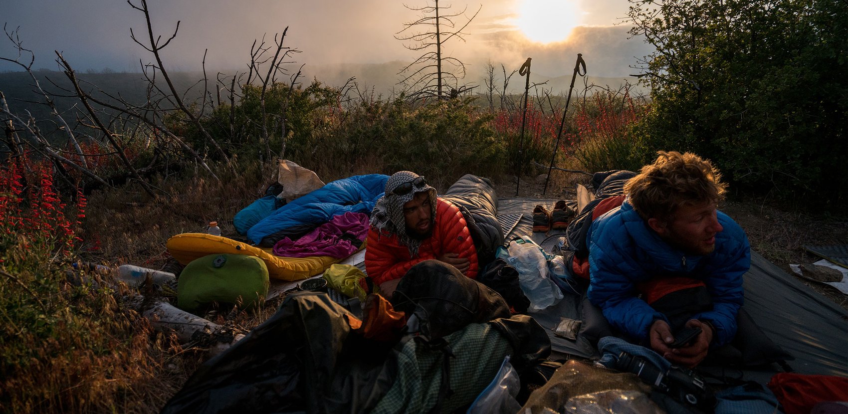 A group of people sitting on the ground in their sleeping bags.