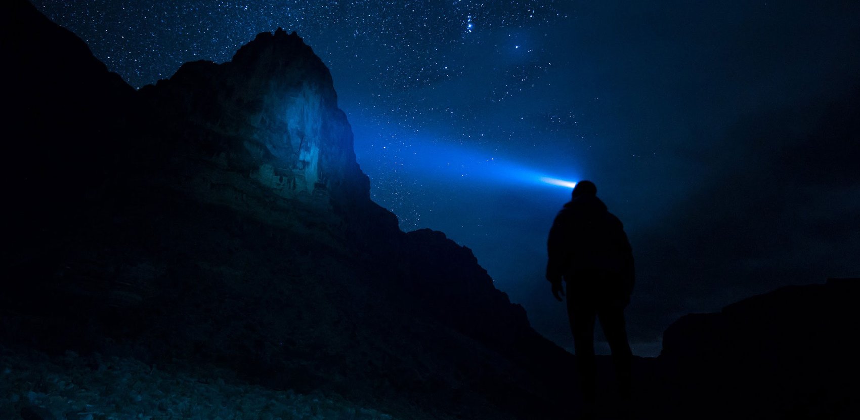 A person standing on a mountain with a blue light shining on him.