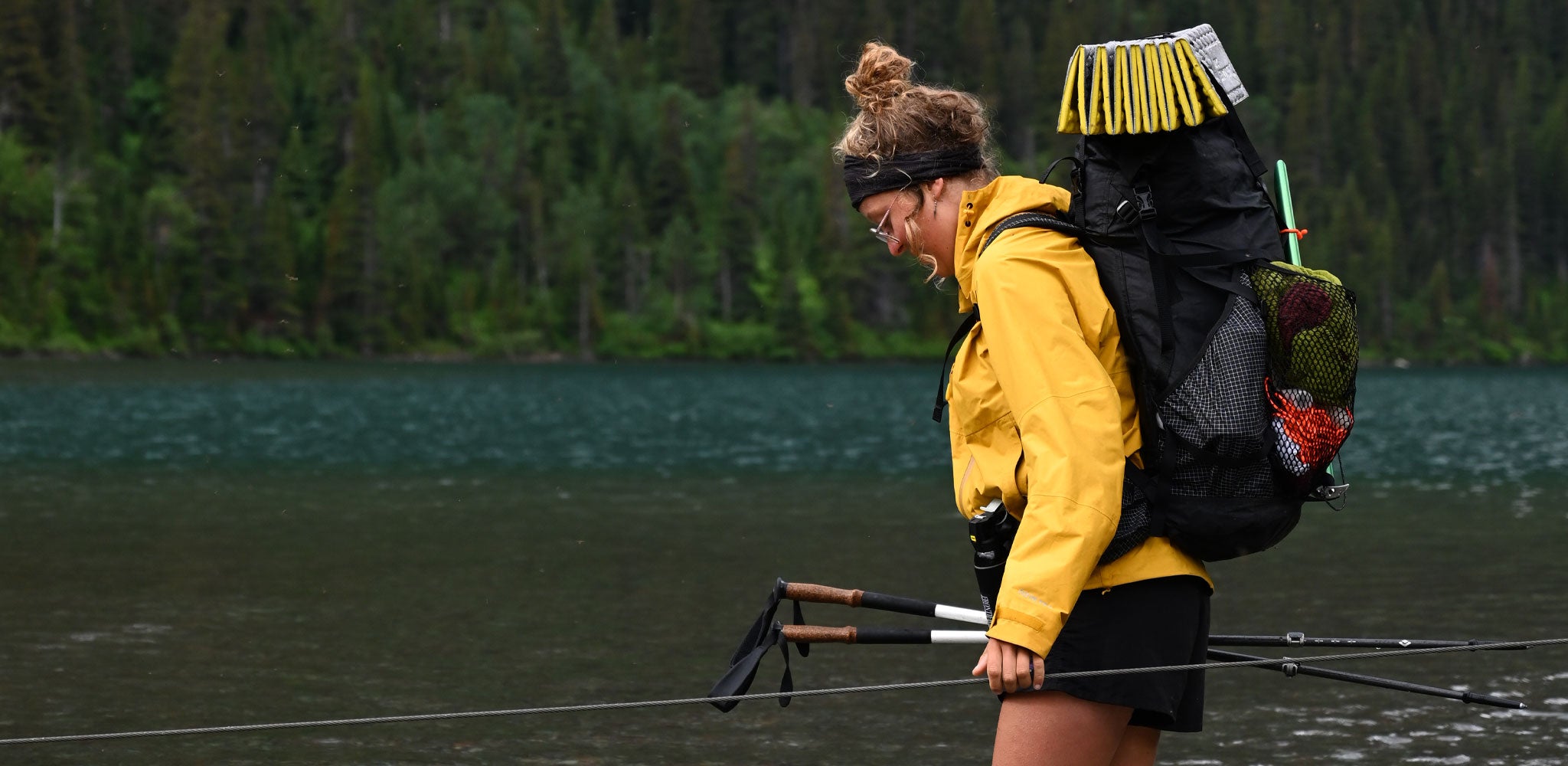 A woman with a backpack and fishing rod on a lake.
