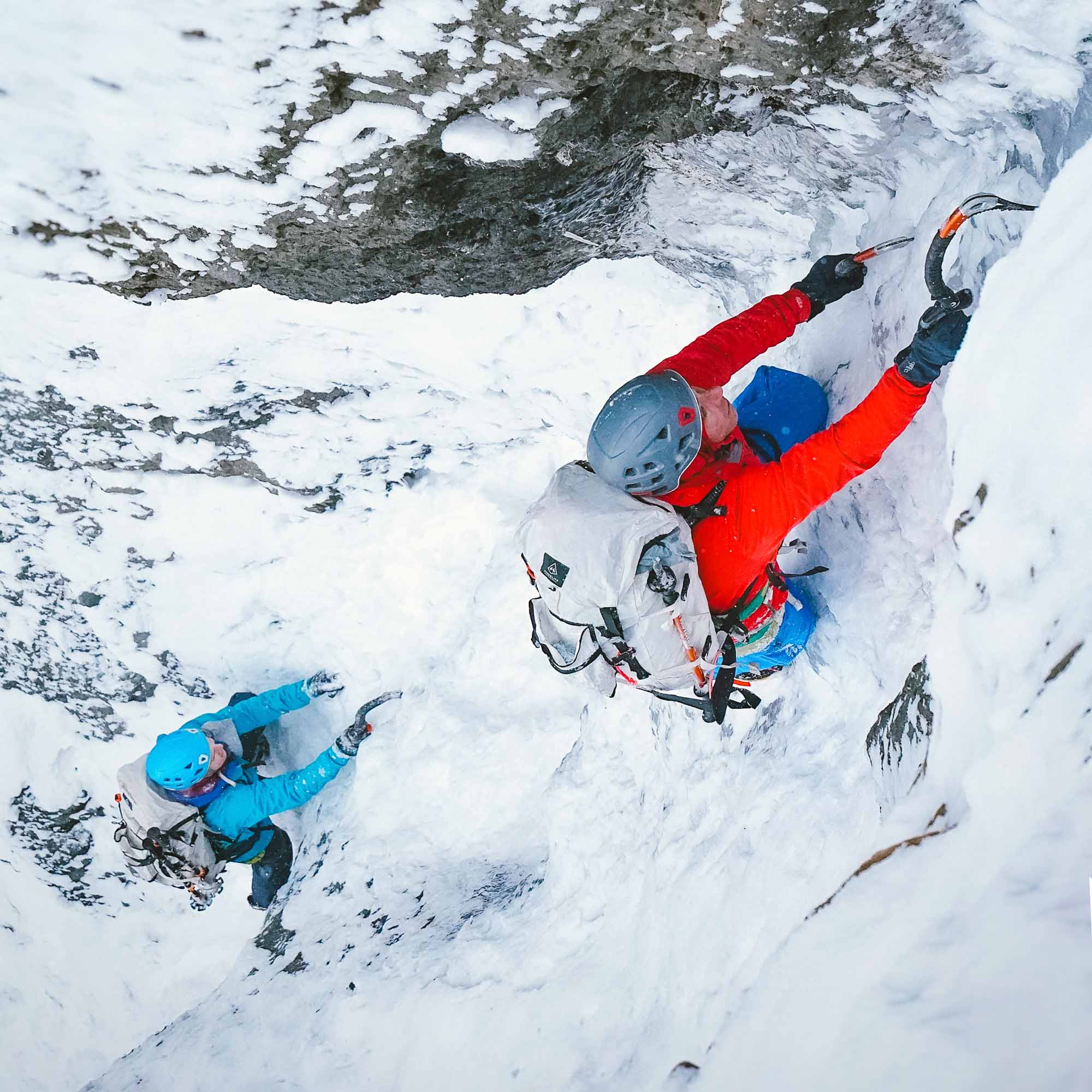 Two people climbing up a snowy cliff.