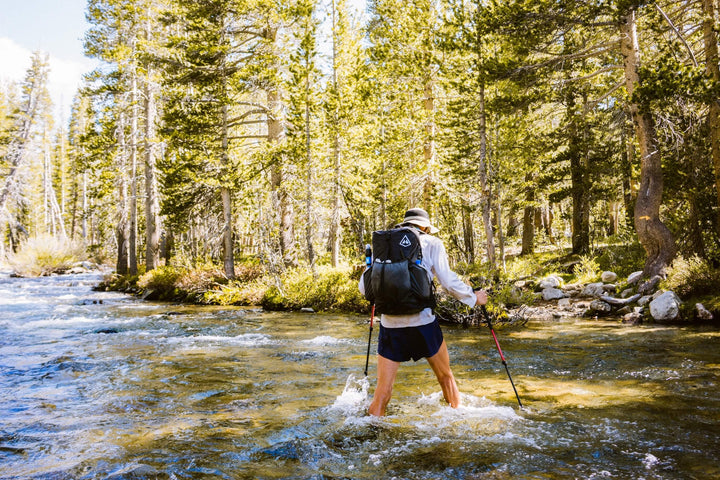 A hiker crossing a river with a backpack.