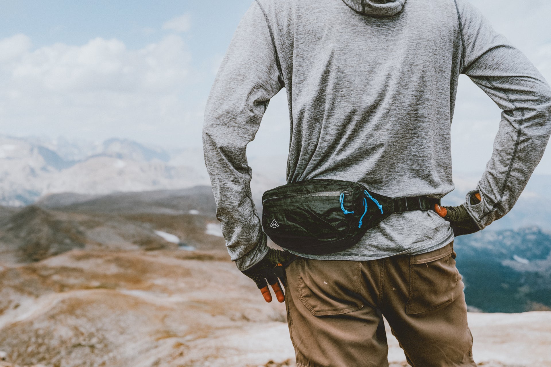 A man standing on top of a mountain with a fanny pack.