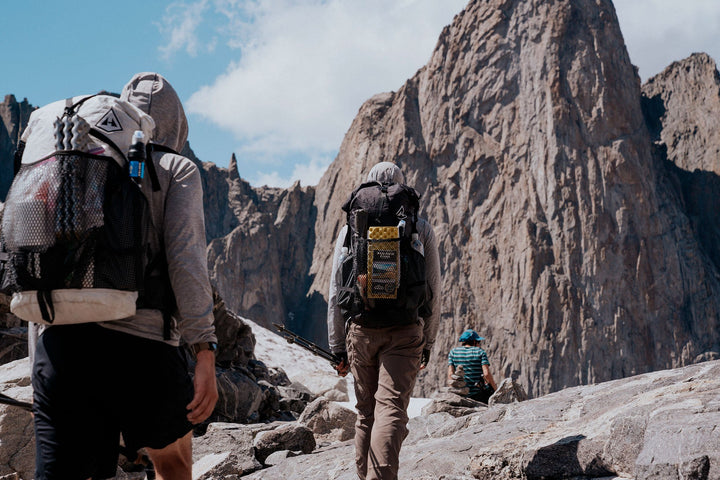 Two hikers with backpacks walking up a rocky mountain.