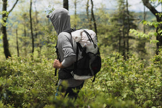 A man walking through the woods with a backpack.