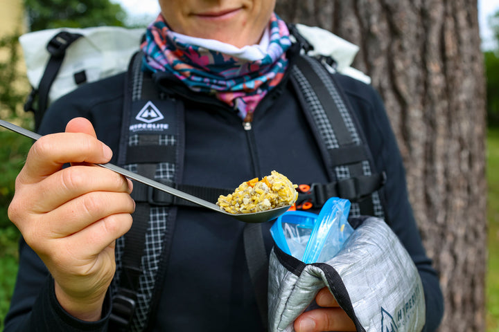 A hiker uses the Vargo titanium long handle spoon to eat food out of the Hyperlite Mountain Gear RePack