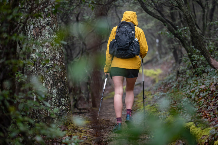 A woman in a yellow jacket hiking in the woods.