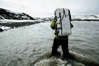 A man carrying a large backpack through a river.