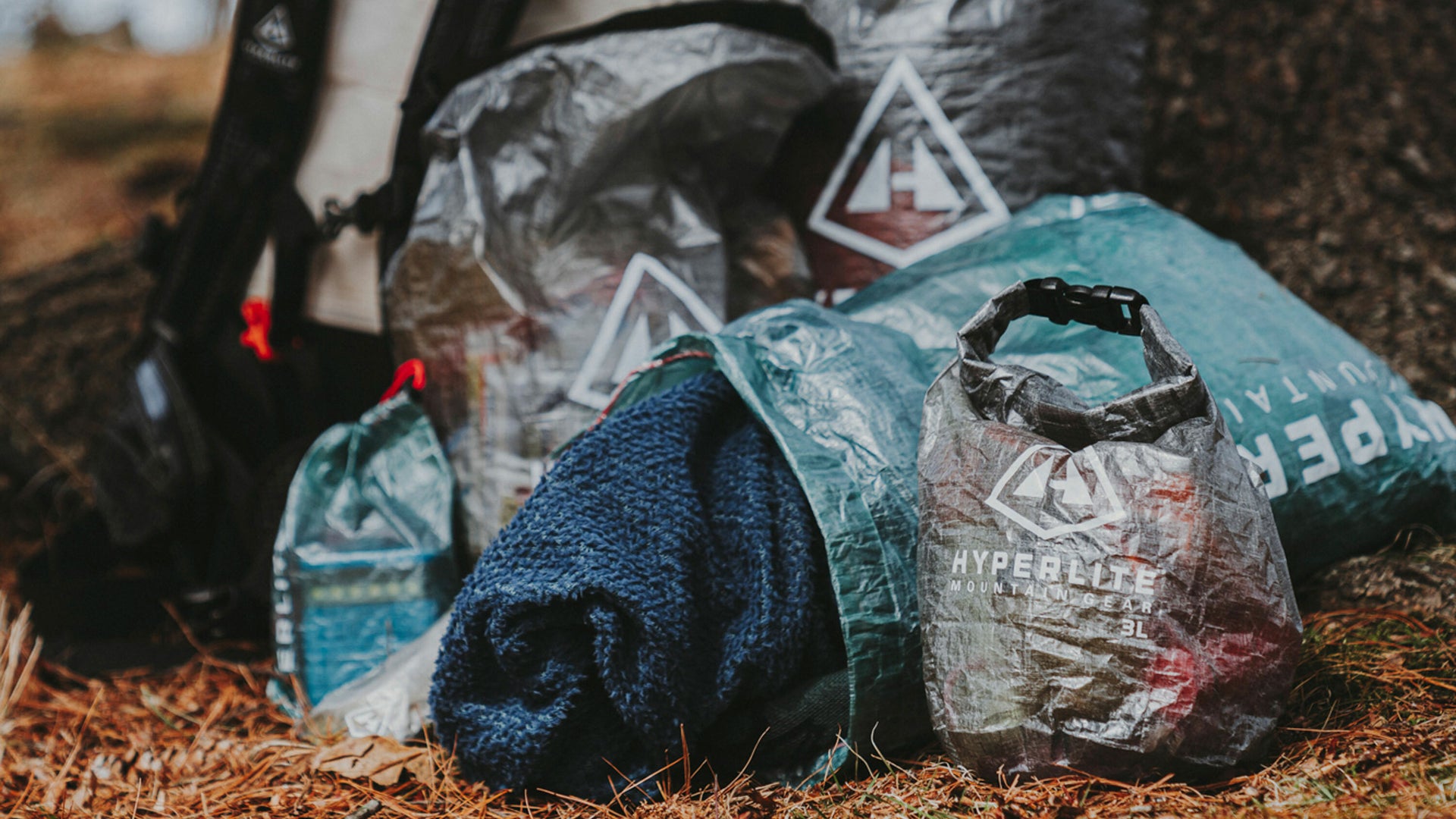 Bags and clothing with recycling symbols on them, placed on a forest floor, indicating an outdoor clean-up or recycling effort.