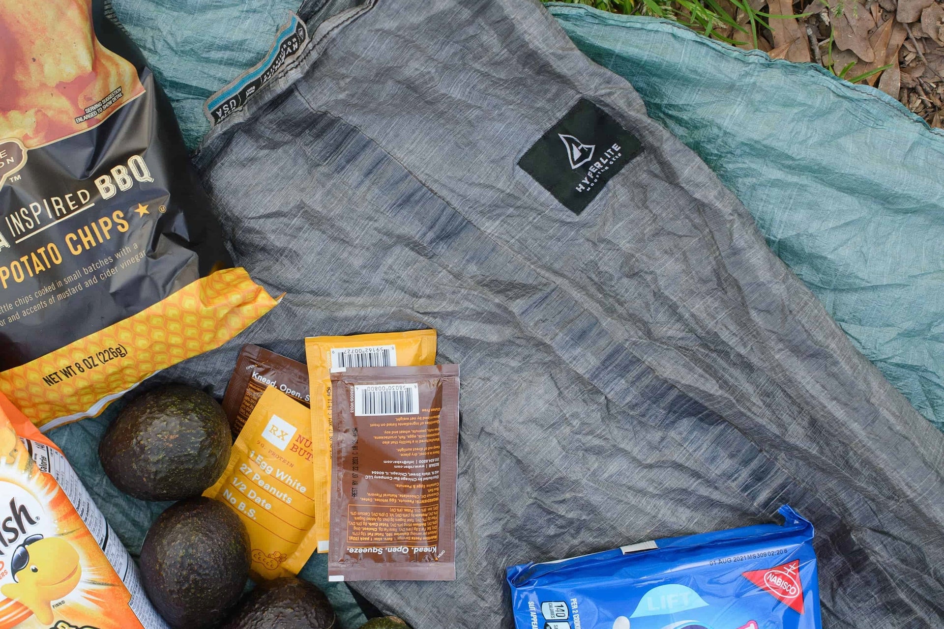 A sleeping bag, snacks, and other items are laid out on the ground.