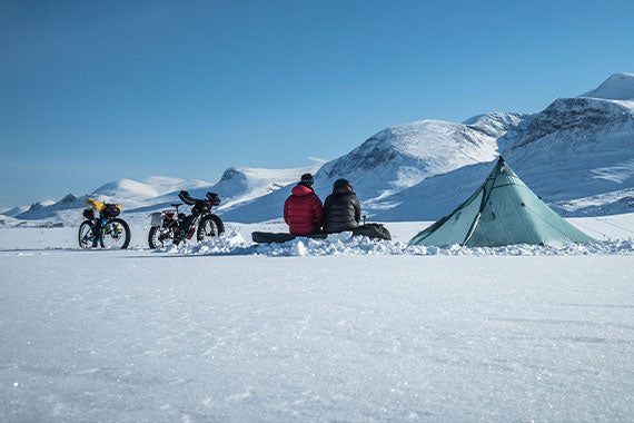 A group of people are sitting in front of a tent in the snow.