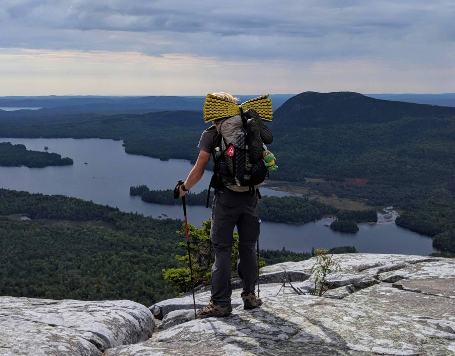 A hiker standing on top of a mountain overlooking a lake.