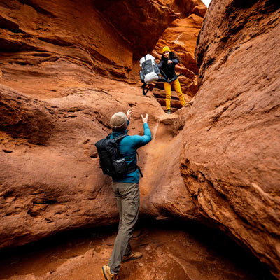 Hiker tosses their Hyperlite Mountain Gear Elevate 22 down to a friend in a narrow sandstone slot canyon