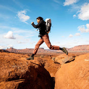 A hiker leaps across a gap on Sandstone terrain wearing the Hyperlite Mountain Gear Elevate 22