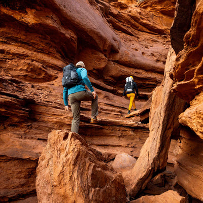 Hikers step up through a sandstone slot canyon wearing the Hyperlite Mountain Gear Elevate 22