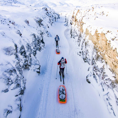 Two people trek through the snow using skis while hauling the Hyperlite Mountain Gear 140L Approach Duffel in sleds behind them