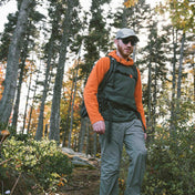 Hiker wearing an orange and grey mid layer traverses the tall pines with the Hyperlite Mountain Gear Unbound 40 Pack
