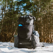 A fully packed Hyperlite Mountain Gear Unbound 40 Pack in Black sitting on snow with trees in the background