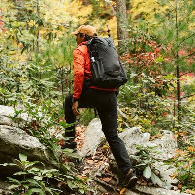 Hiker steps up a rocky trail surrounded by trees and shrubs wearing the Hyperlite Mountain Gear Waypoint 35