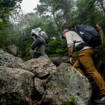 Two Hikers ascend a small rock scramble on a rocky and tree covered trail wearing their Hyperlite Mountain Gear Waypoint 35's