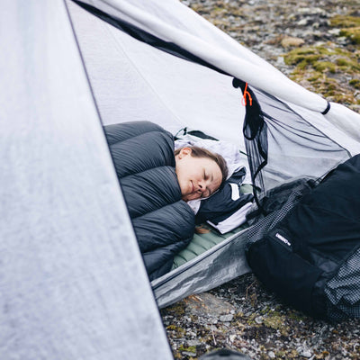 A camper sleeps inside of the Hyperlite Mountain Gear Mid 1 Tent in broad daylight with the vestibule door open