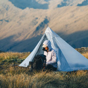 A camper sitting outside of their Hyperlite Mountain Gear Mid 1 with a mountain backdrop