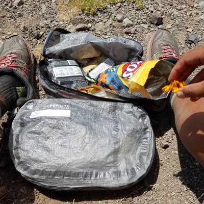 A hiker pauses to open their Hyperlite Mountain Gear Pods with snacks inside 