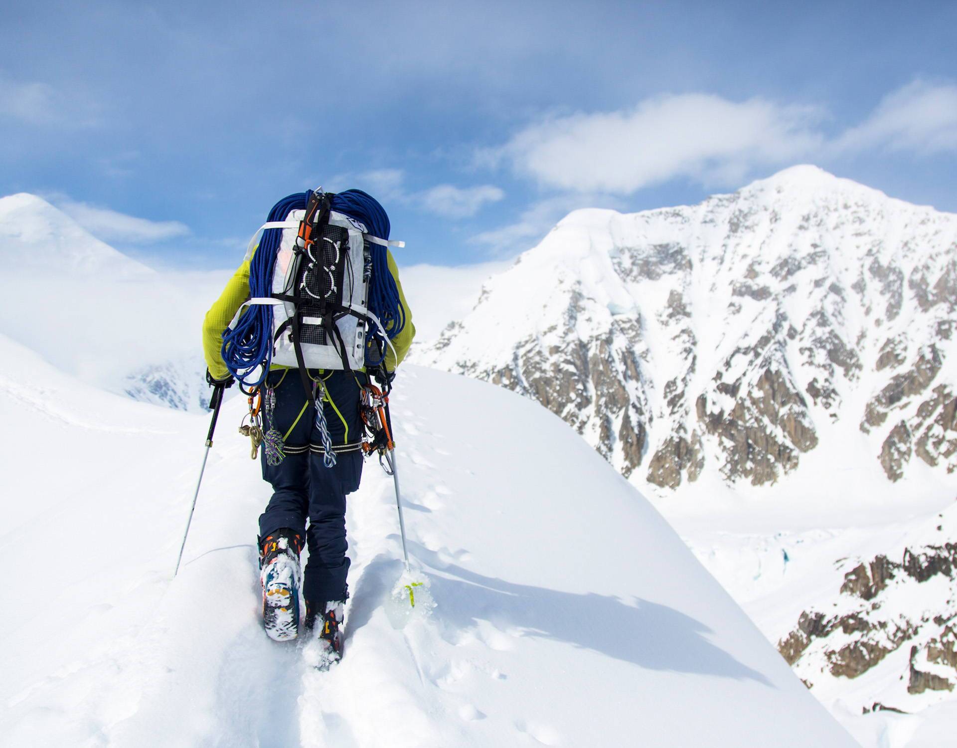 A man is hiking up a snowy mountain with skis on his back.