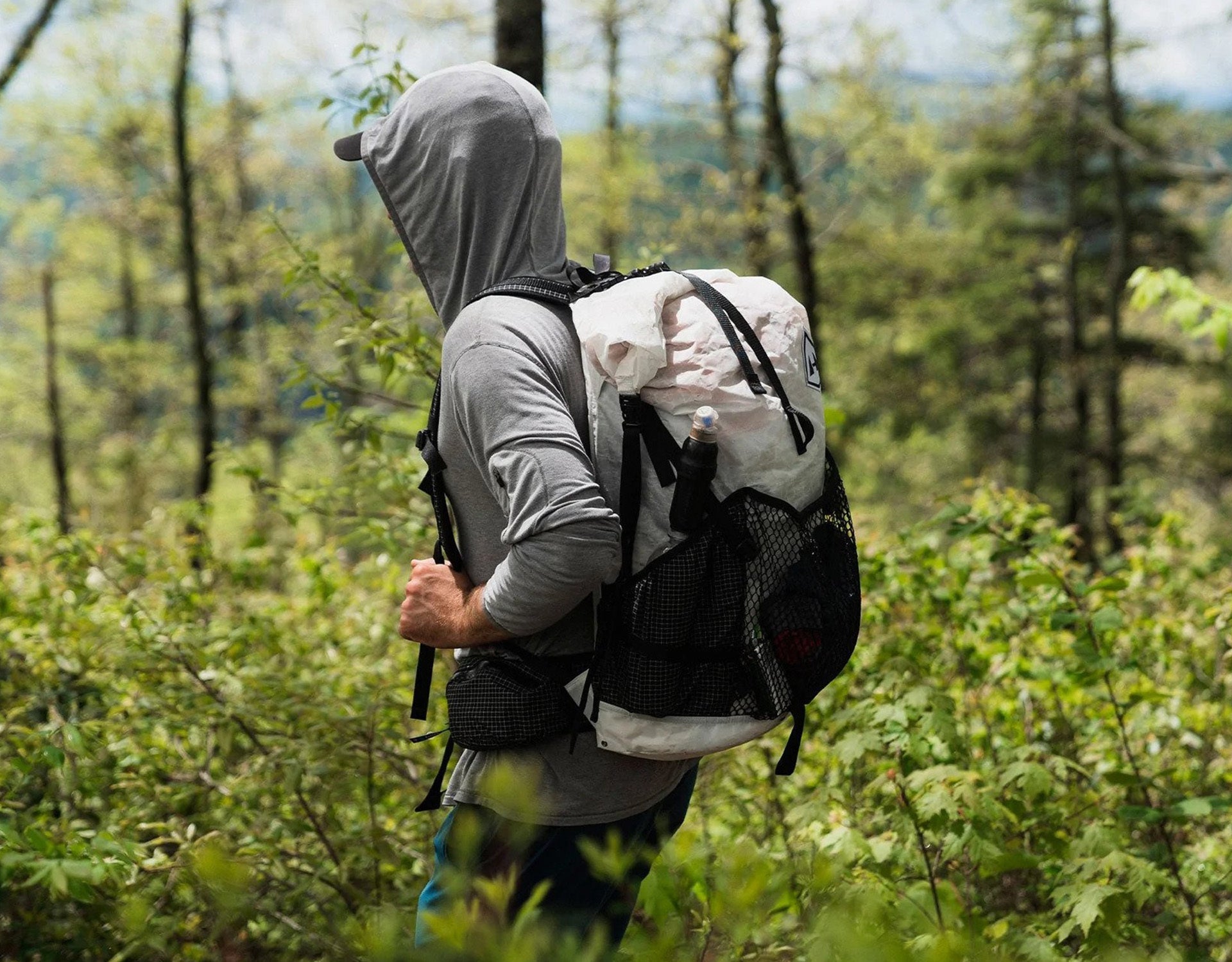 A man walking through the woods with a backpack.