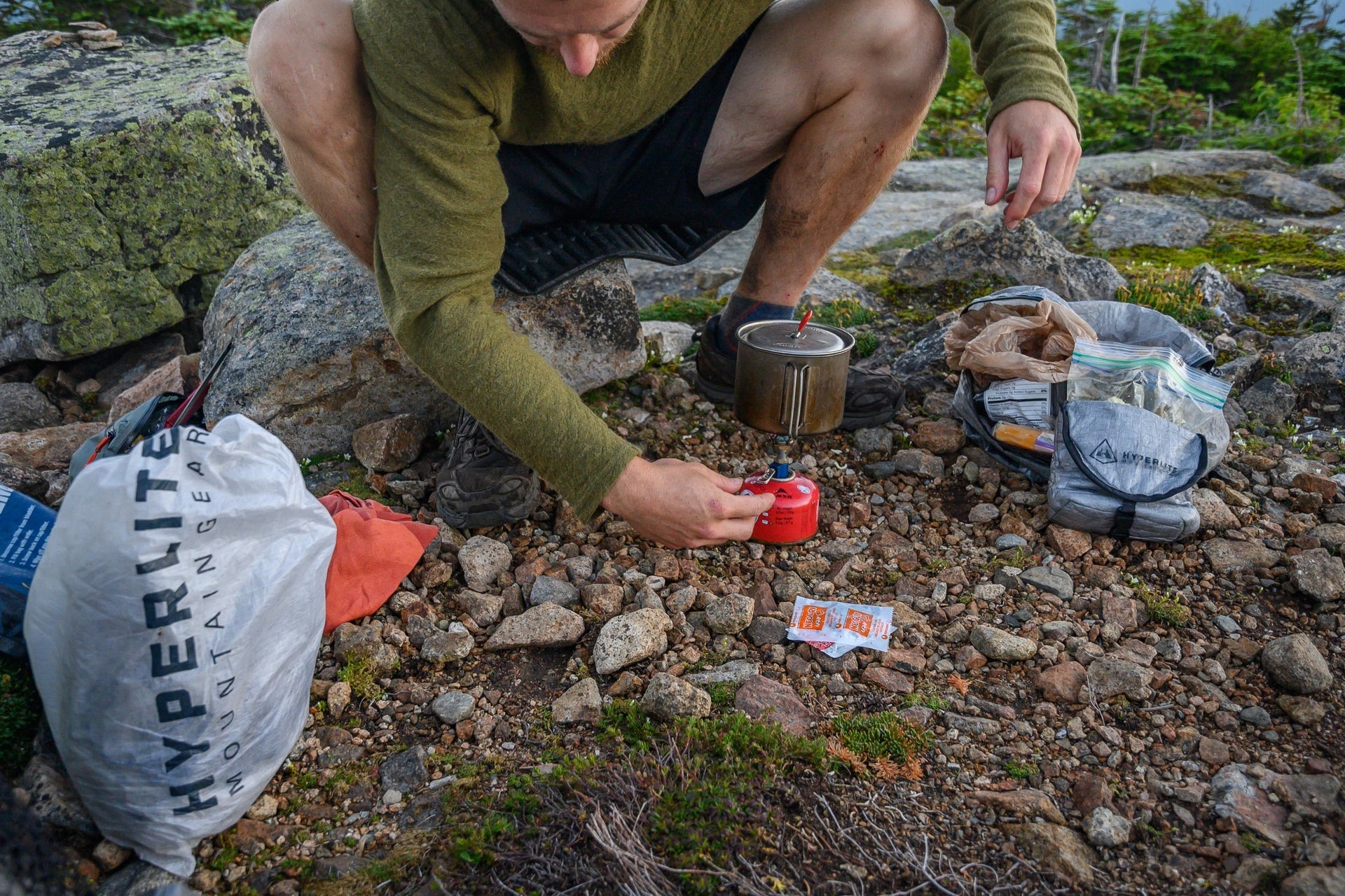 A man is preparing food on a rock in the mountains.