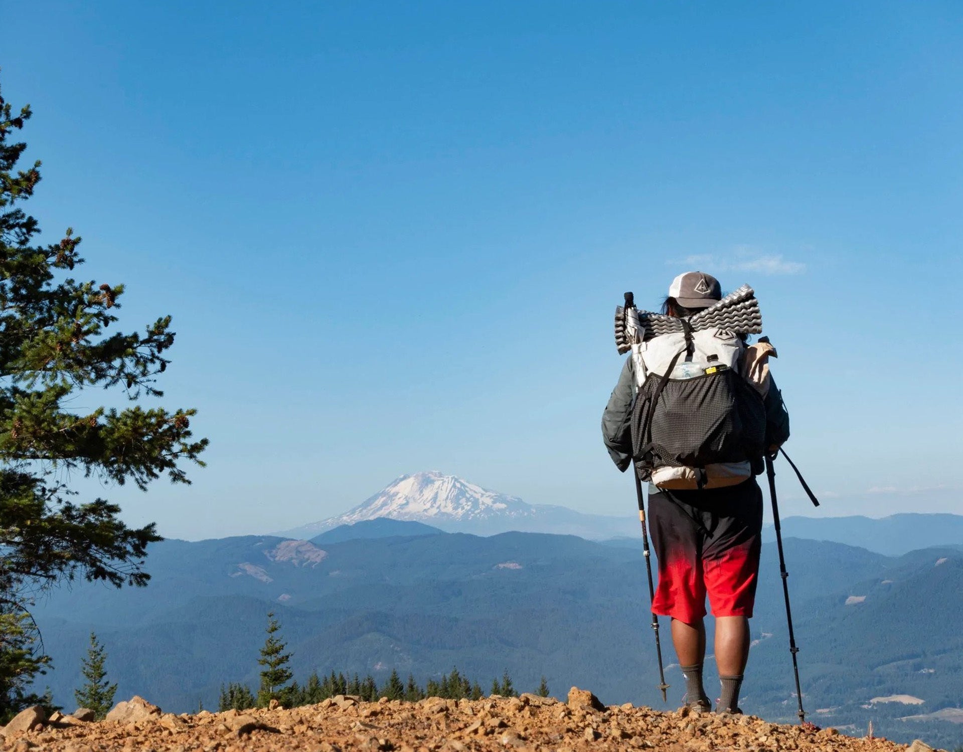 A man with backpack and hiking poles standing on top of a mountain.