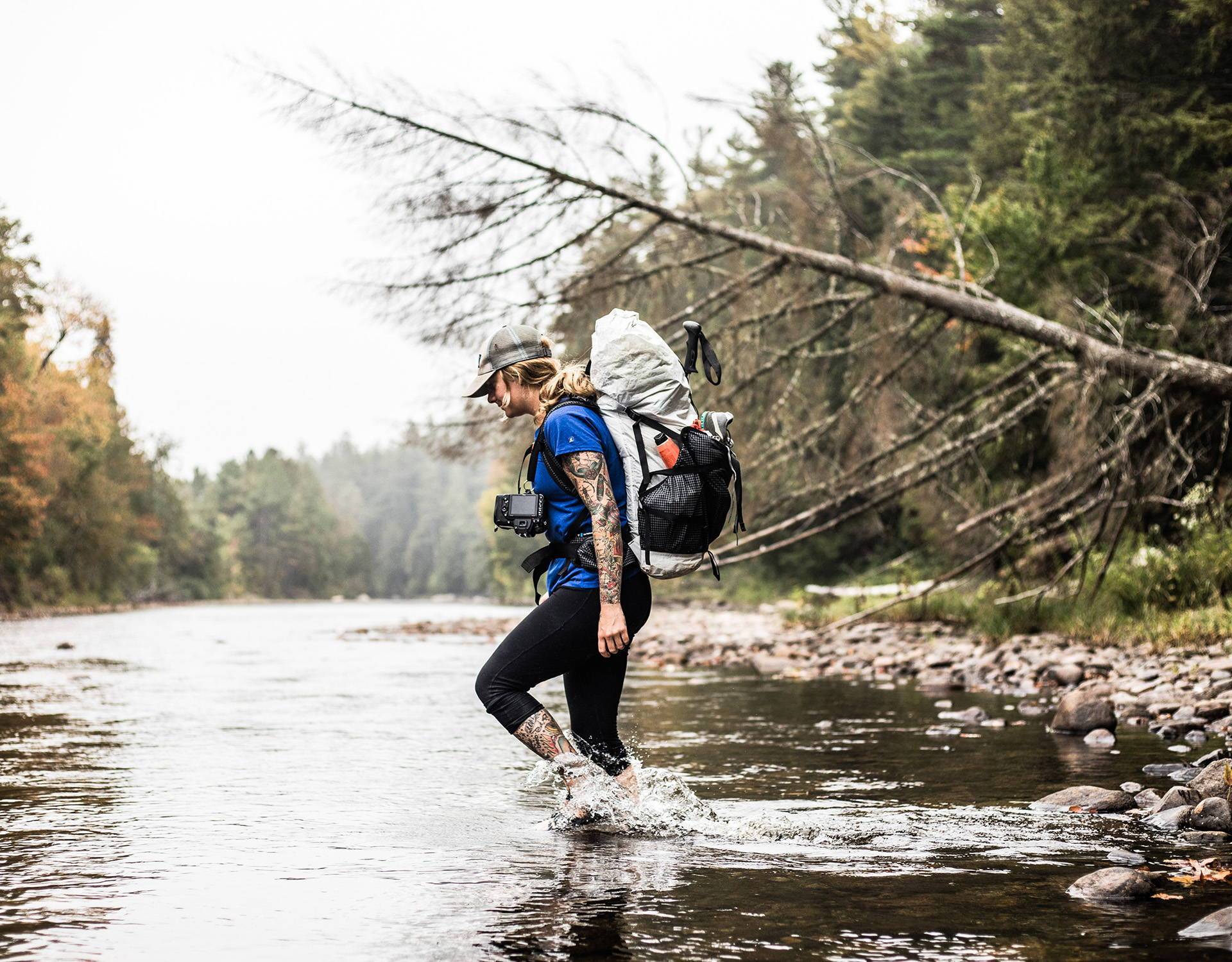 A woman crossing a river with a backpack.