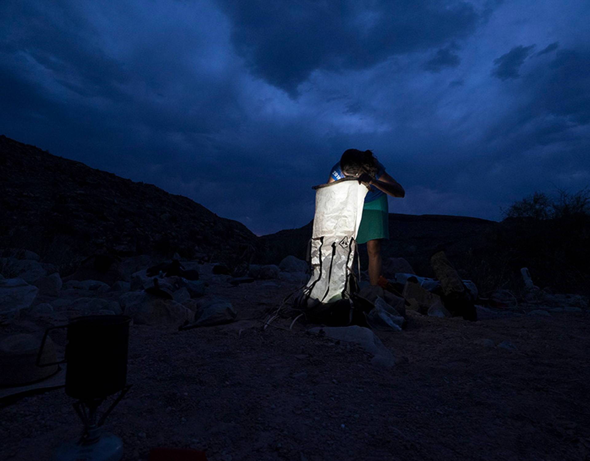 A woman is standing in the desert at night with a flashlight.