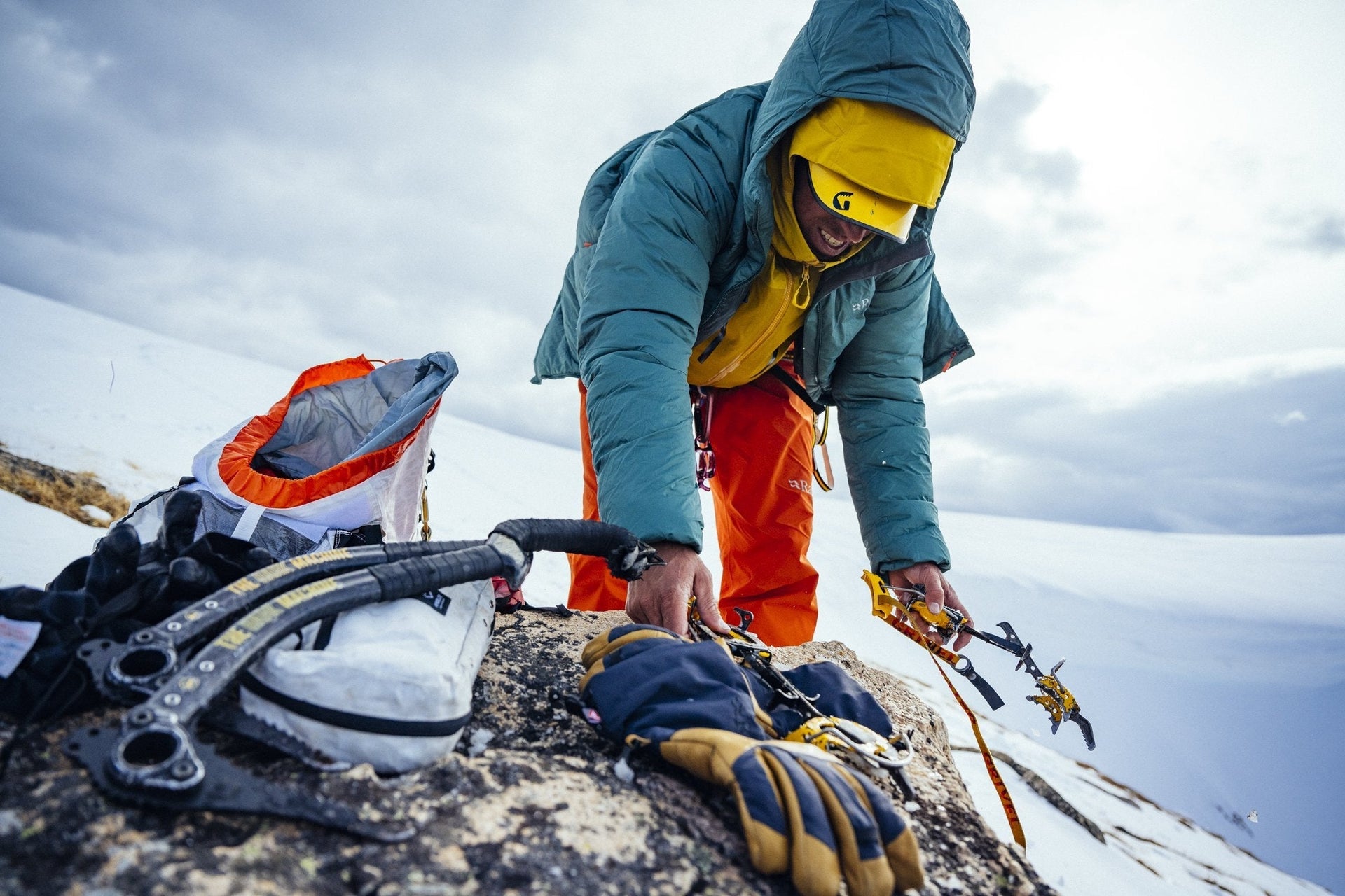 A man is preparing his gear on top of a snowy mountain.
