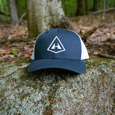 Front view of Hyperlite Mountain Gear's Trucker Hat in Navy and White on a rock