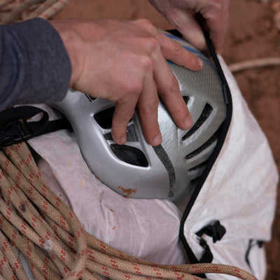 Hiker placing a helmet in the exterior pocket of Hyperlite Mountain Gear's NorthRim 70 Pack in White