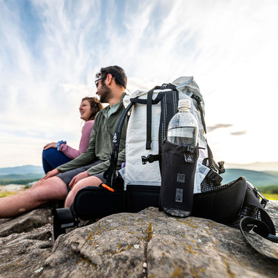 Hyperlite Mountain Gear's The Bottle Pocket in Black attached to backpack shoulder straps on a mountain