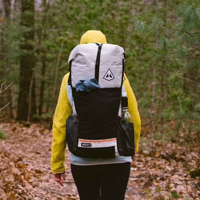 A hiker wearing the Hyperlite Mountain Gear Unbound 55 in white starts down a forested trail covered in leaves