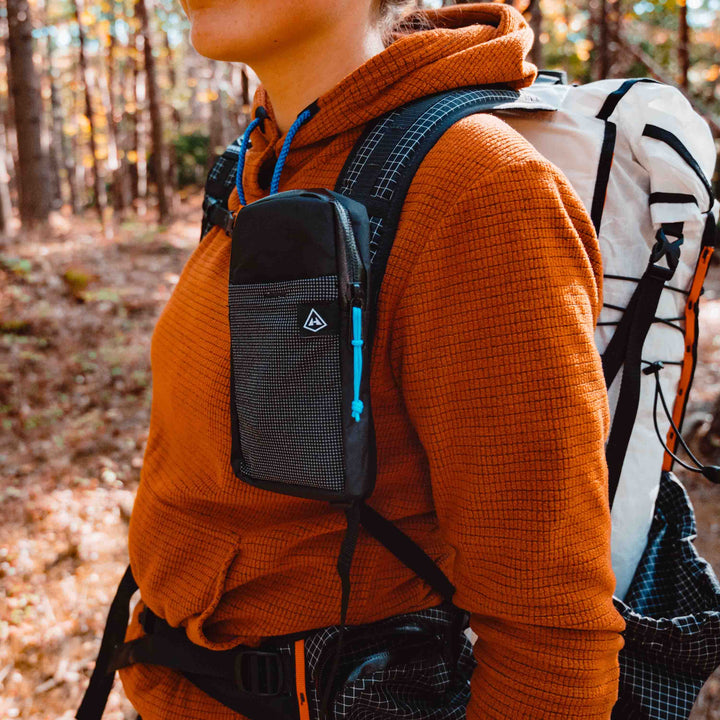A woman with a backpack in the woods holding a cell phone.