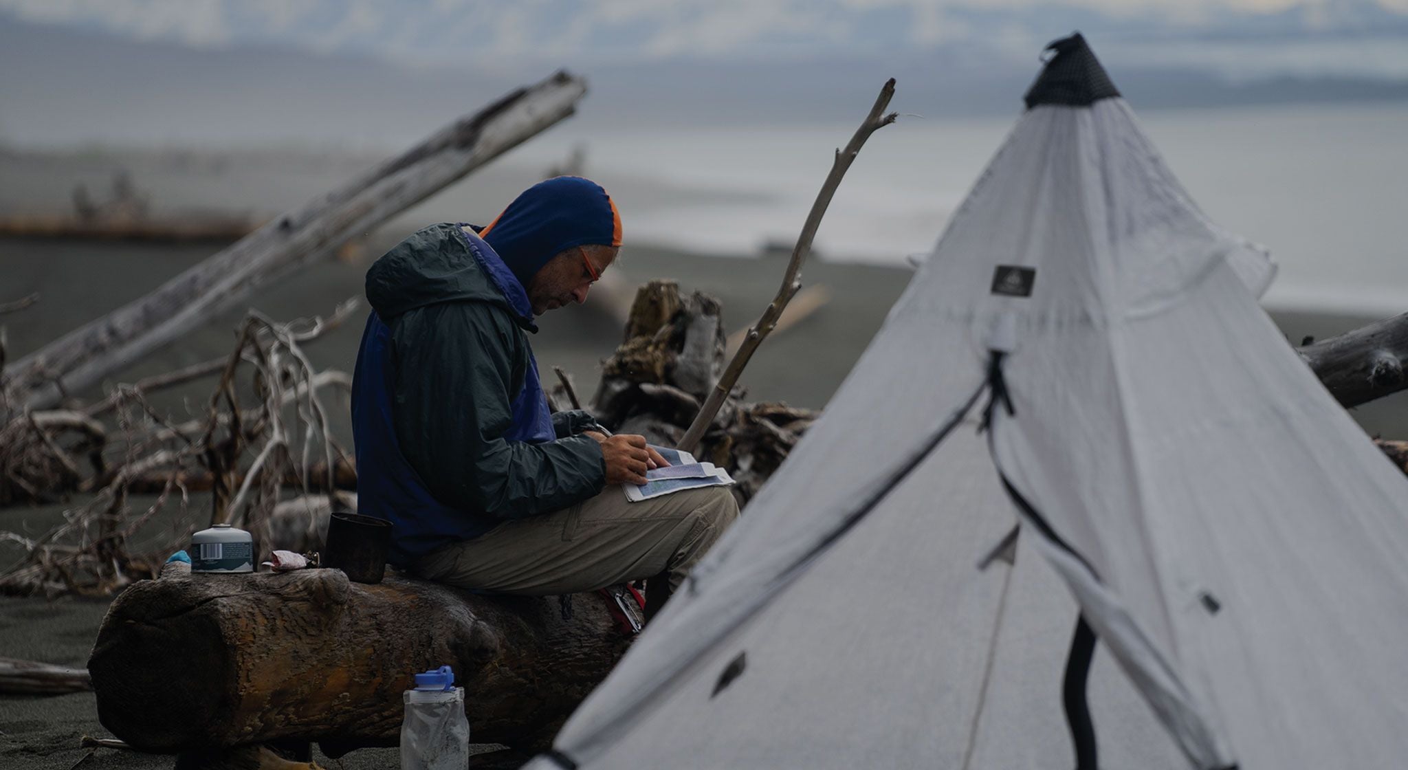 A man sits in front of a tent with a notebook.