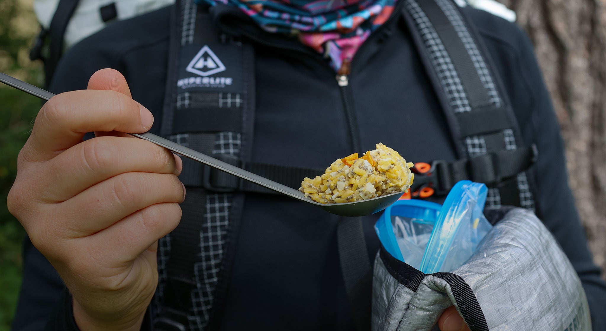A person holding a spoon full of food in a backpack.