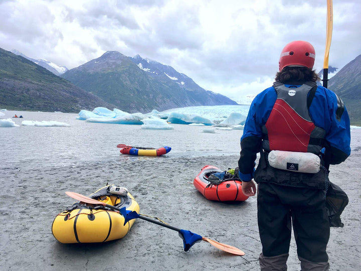 A man stands next to a group of rafts and a glacier.