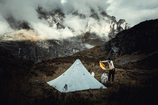 A man standing next to a tent in the mountains.