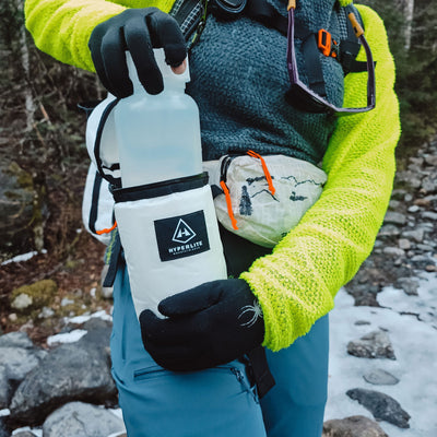 A person in winter gear removes their water bottle from the Hyperlite Mountain Gear Insulator attached to their harness