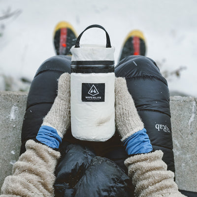 A person holding the Hyperlite Mountain Gear Insulator in their lap as they sit in snowy terrain
