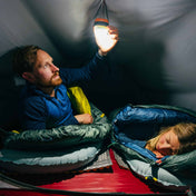 A camper lays on the Therm-a-Rest NeoAir® XTherm™ NXT Sleeping Pad in their tent while turning on an overhead lantern