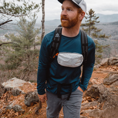 A hiker wears the Hyperlite Mountain Gear Accessories Vice Versa in White attached to their pack