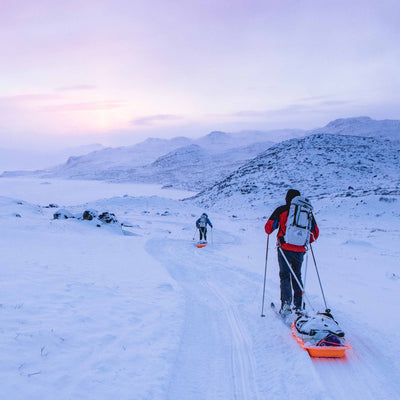 A skiier approaches basecamp on skis with their Hyperlite Mountain Gear 140L Approach Duffel in a sled behind them