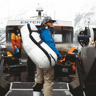 A person standing on a boat with the Hyperlite Mountain Gear 140L Approach duffel slung over their shoulder