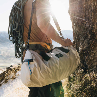 A climber with a rope slung over their back carries the Hyperlite Mountain Gear 30L Approach Duffel to the base of a climb