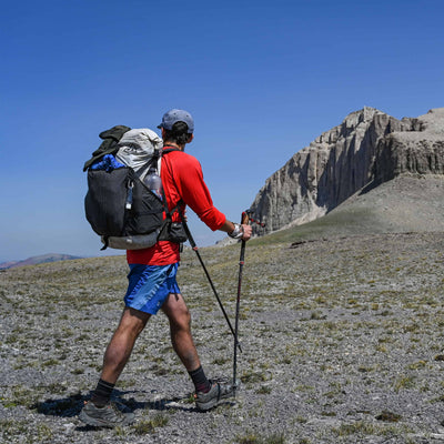 Adventurer equipped with the Southwest 55 backpack and trekking poles traversing a sandy landscape